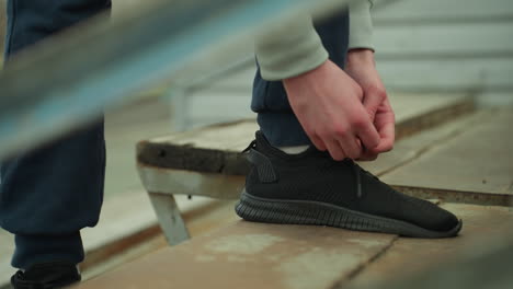 close-up of someone tying his shoelace on a rusty staircase, with a blurred view of someone in a brown sweater walking in the background