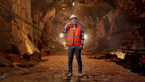full body of asian male engineer with safety helmet smiling to camera and making call me gesture while standing in underground mine tunnel