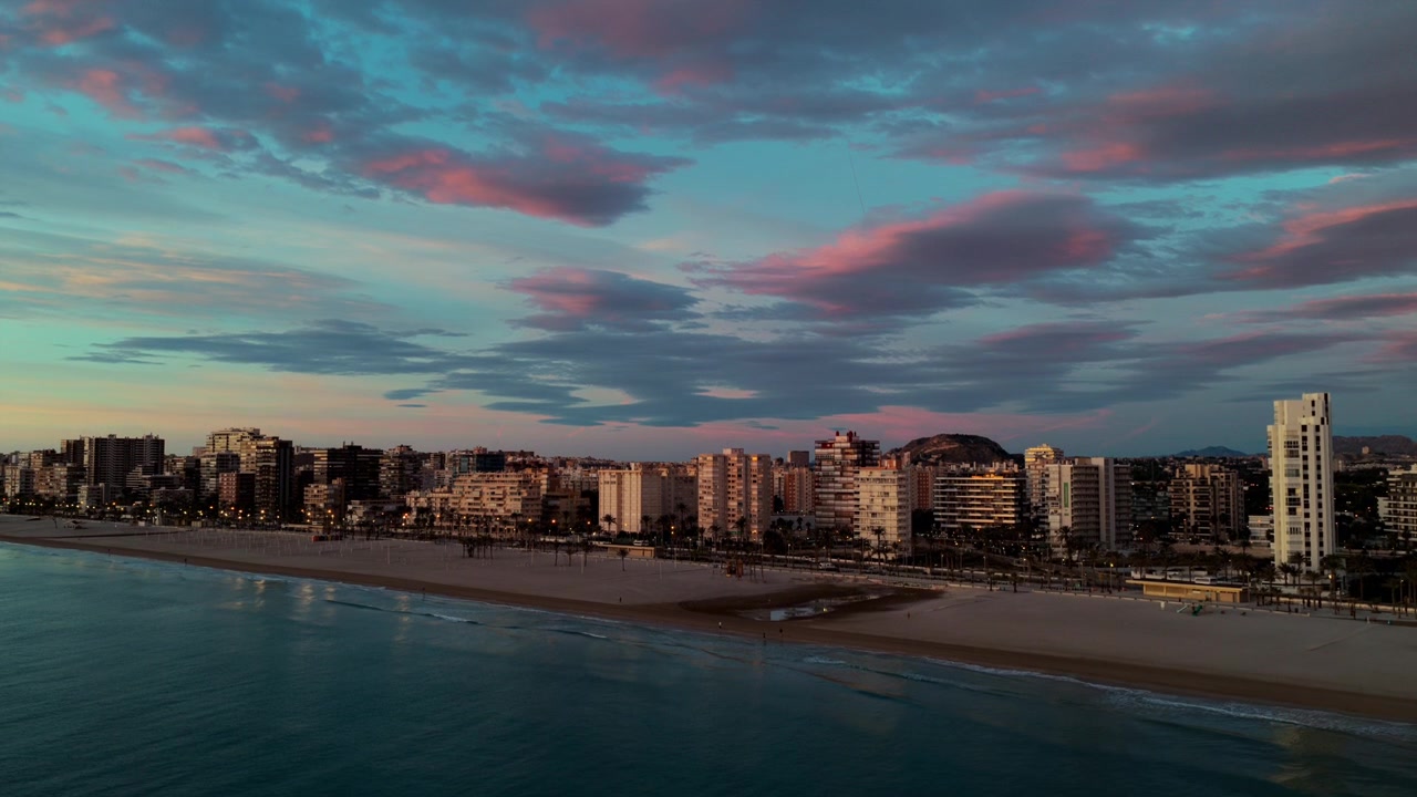 Città di Alicante e la sua lunga spiaggia sabbiosa durante il crepuscolo colorato dell'ora blu in Spagna. Drone aereo in ascesa, spazio per il testo