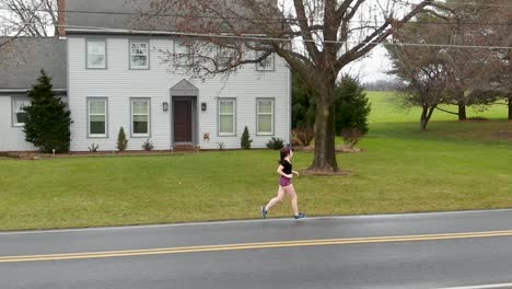 Slow-motion-of-a-young-woman-running,-female-teenager-trains-for-race-on-road-beside-traditional-family-home-in-Lancaster,-Pennsylvania,-USA