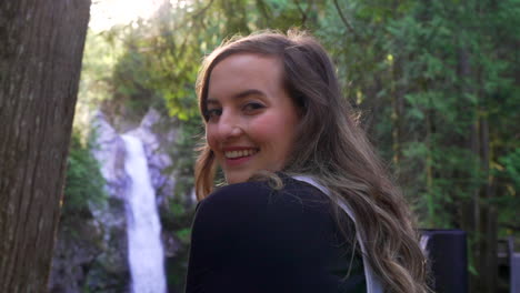 mujer mirando a la cámara cruzando el viejo puente tradicional en el bosque en columbia británica bc, canadá con cascada y río