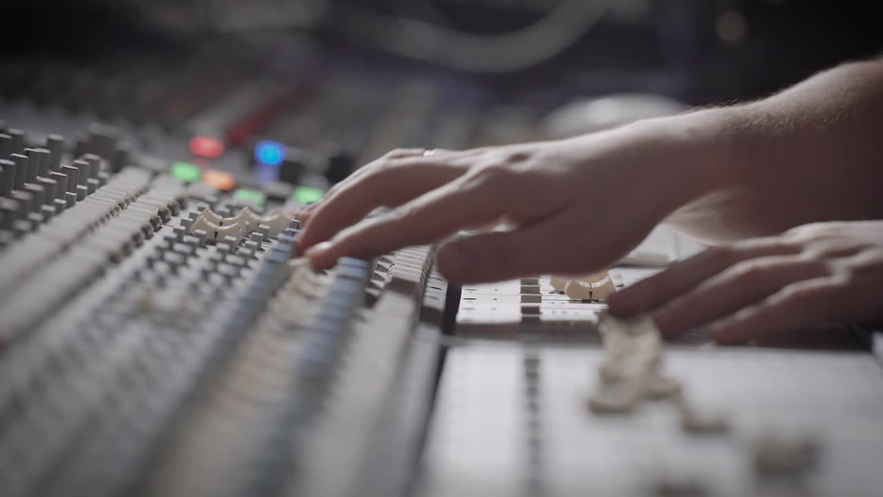 Side view shot of a musician working on audio mixing console in a music studio