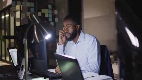 Video-Eines-Afroamerikanischen-Geschäftsmannes,-Der-Nachts-Im-Büro-Am-Schreibtisch-Sitzt-Und-Einen-Computer-Benutzt