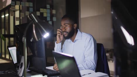 video of african american businessman sitting at desk using computer at night in office