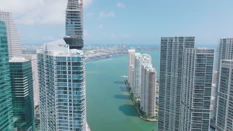 Forwards-fly-between-tops-of-modern-downtown-skyscrapers.--Revealing-view-of-sea-bay-with-cruising-boats.-Miami,-USA
