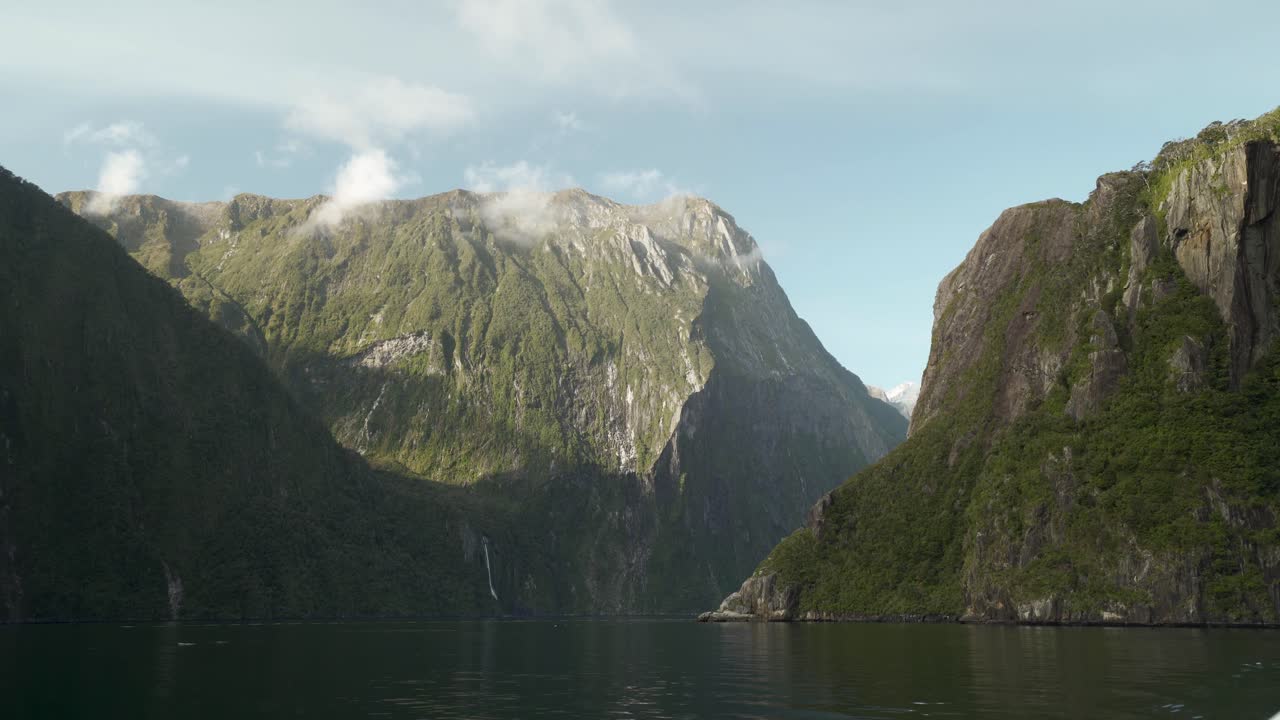 Malownicze ujęcie krajobrazu ogromnych górskich ścian w słońcu, z doliną wodną przepływającą między nimi w nowozelandzkim Milford Sound