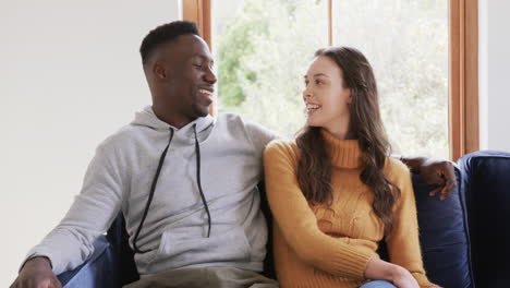 happy diverse couple sitting on sofa talking and smiling in home,copy space