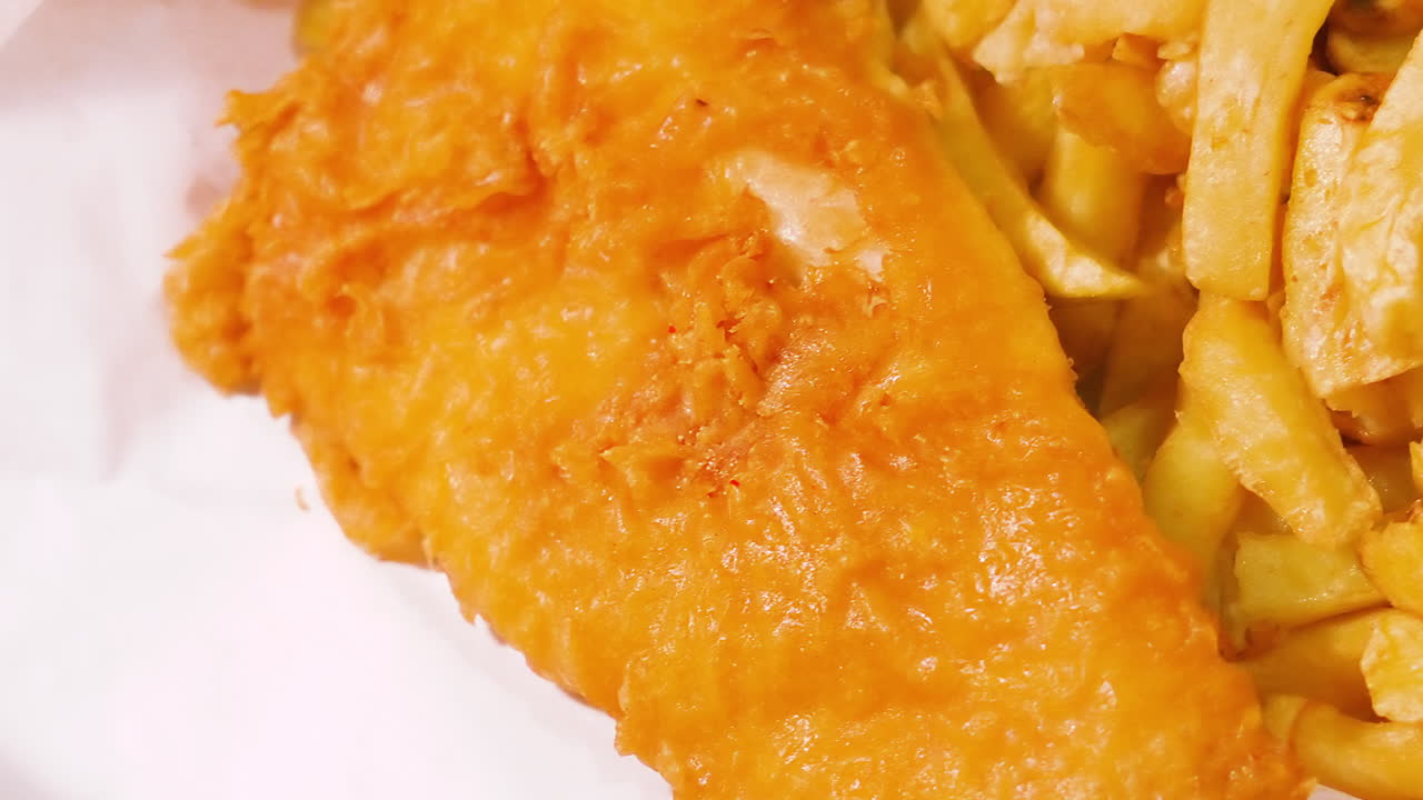 Overview of Delicious British Fish and Chips in Traditional White Paper with Crispy Batter. English Cuisine Takeaway Dinner Food. Deep Fried Fresh Cod Seafood Served in Britain