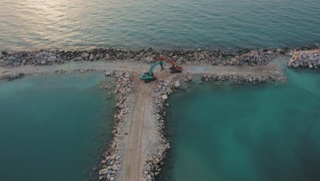 Ein-Flaches-Meer-Bei-Sonnenuntergang-Mit-Zwei-Baggern,-Die-Auf-Einem-Von-Ihnen-Gebauten-Steinpier-Stehen