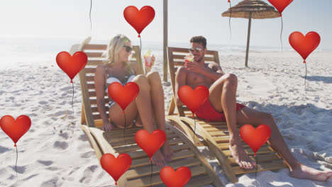 animación de globos de amor de corazón rojo iconos digitales sobre pareja en sillas de sol con bebidas en la playa