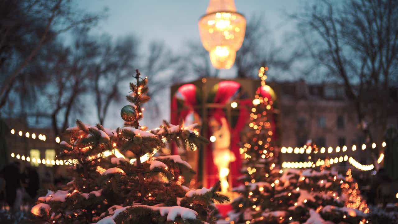 Wide view of a festive Christmas decoration with lights, at an outdoor cafe near small trees, and ornaments
