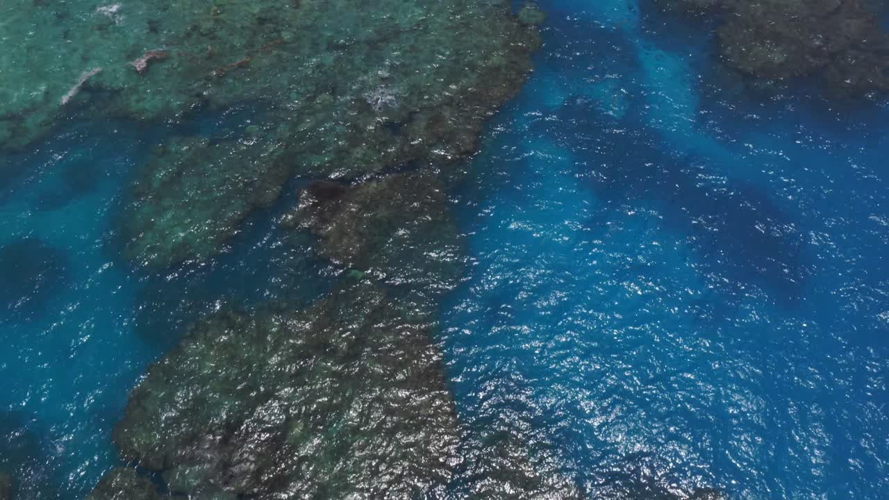 un dron captura una imagen de una laguna azul, mostrando las aguas cristalinas, mientras la cámara se desplaza hacia arriba para revelar el exuberante paisaje costero tropical con una nube lluviosa distante