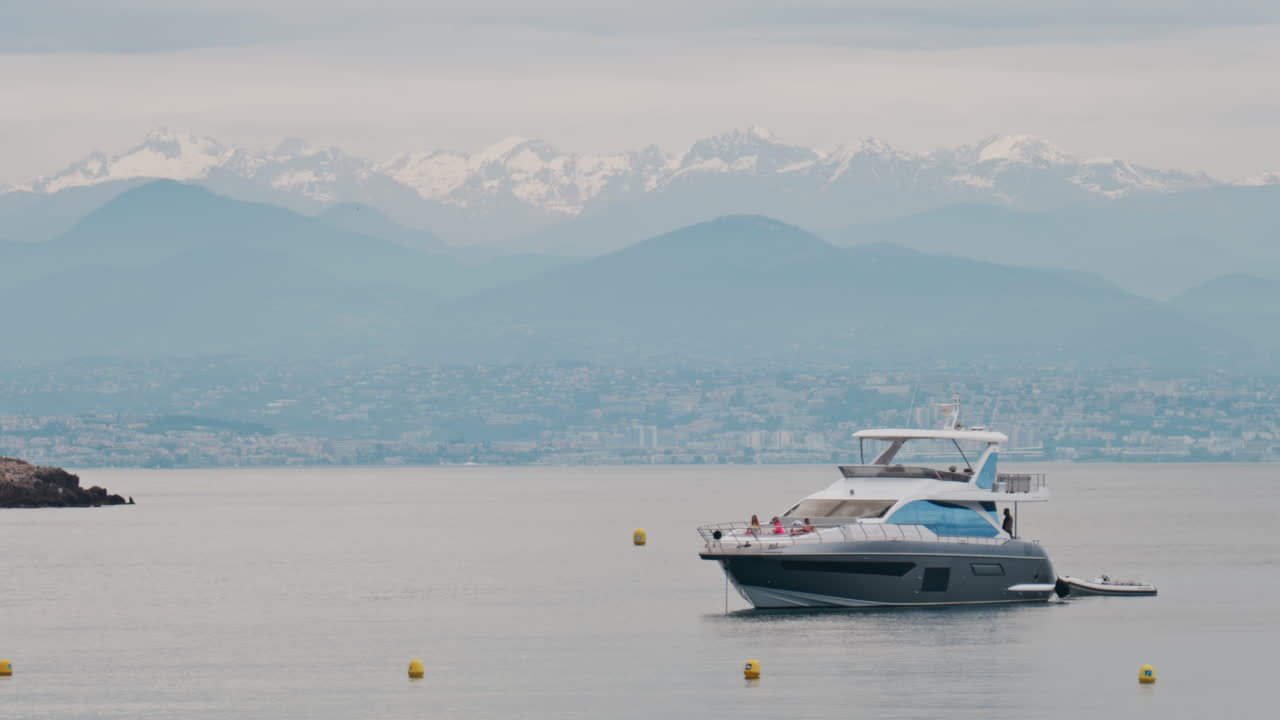 Antibes, Francia - 6 maggio 2025: persone su una barca ormeggiata in mare, con la città e le montagne sullo sfondo in pieno giorno