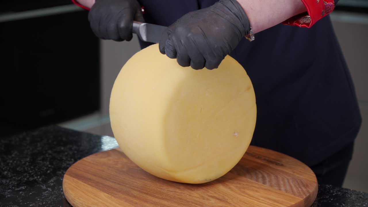 Mani di donna tagliano un pezzo di formaggio rotondo con un grande coltello. Un operaio di caseificio taglia formaggio fresco appena prodotto