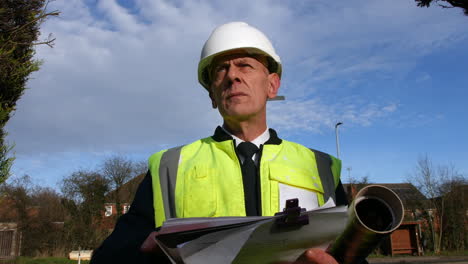 Primer-Plano-Retrato-De-Un-Arquitecto-Gerente-De-Construcción-De-Edificios-En-Una-Calle-Residencial-Con-Tráfico-Y-Casas-Mirando-El-Papeleo-Inspeccionando-El-Edificio