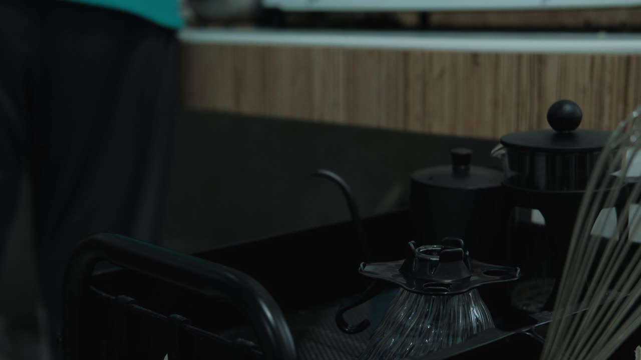 Static close-up shot of young man placing coffee-making gear on cart in kitchen.