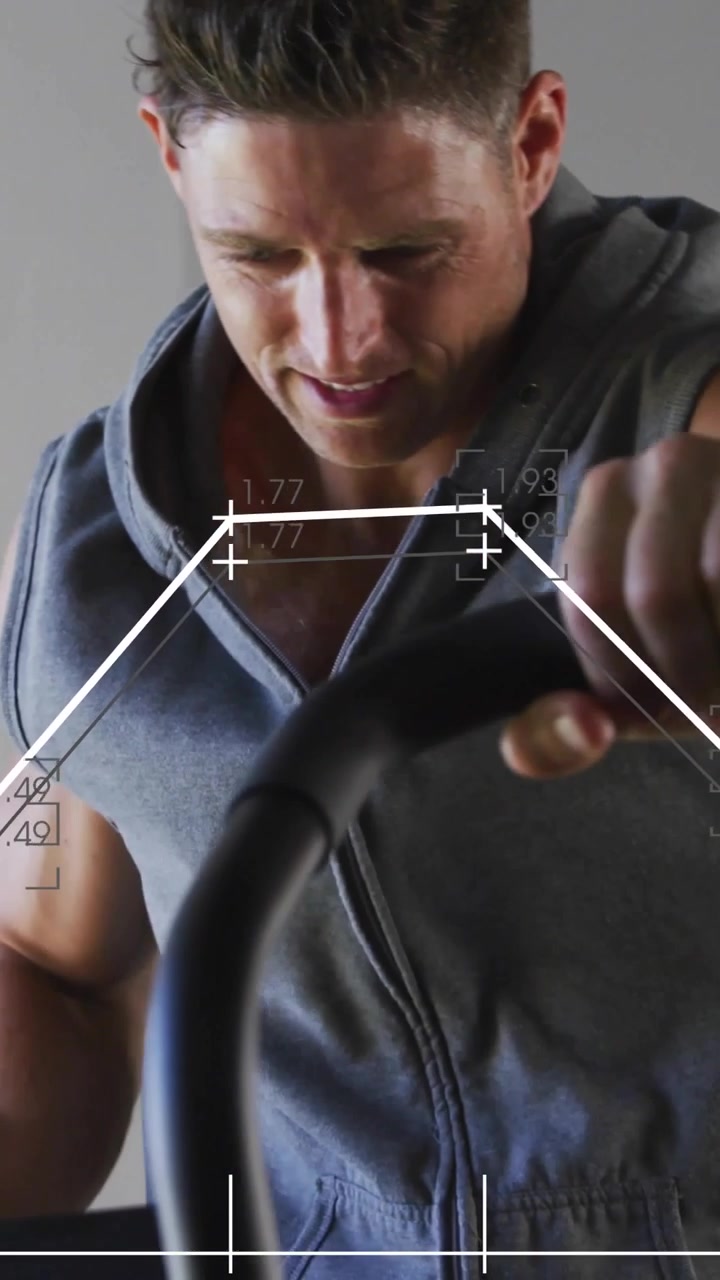 Vertical video: Leaning man in sleeveless hoody pedaling in studio, data causing grip adjustments