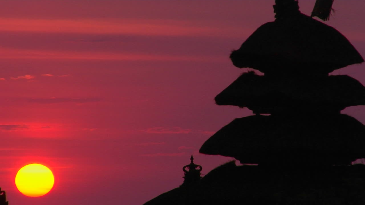 Il Tempio Pura Tanah Lot si staglia in silhouette contro un cielo luminoso.