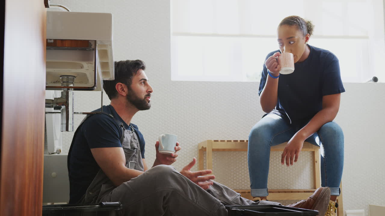 Male Plumber With Female Apprentice Taking A Break From Fixing Leaking Sink In Home Bathroom