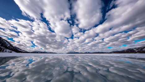 frozen lake with reflection of clouds and mountains