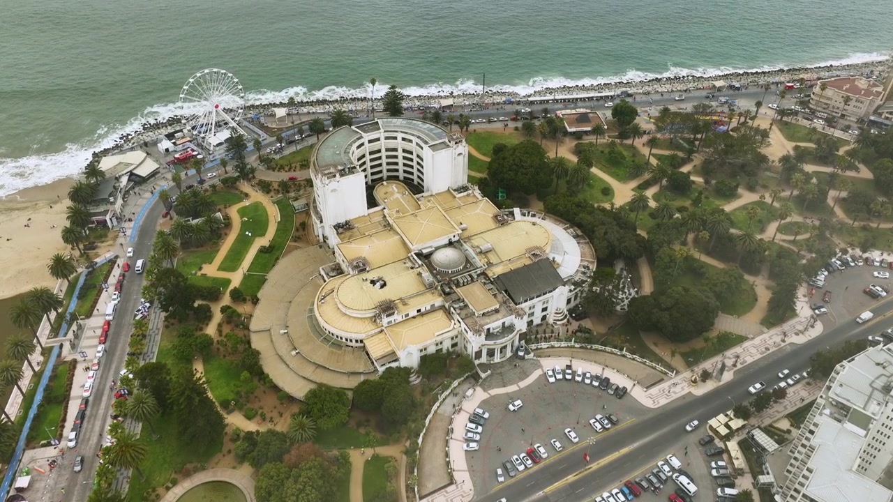 Un volo panoramico in avanti con drone che inizia con una vista aerea dall'alto di edifici e parchi di una città costiera, spostandosi verso l'Oceano Pacifico a Viña del Mar, Cile.