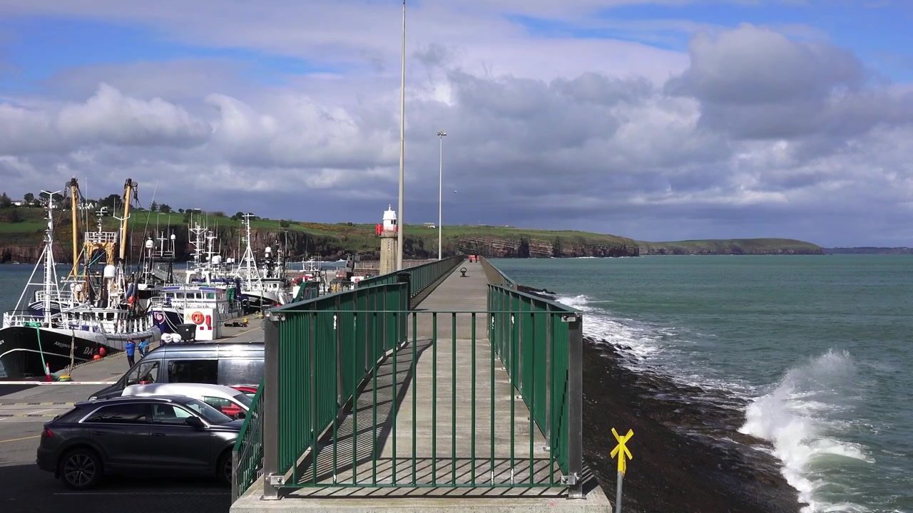 Trålare i skydd bakom vågbrytaren med gångväg ovanpå och fyr vid ingången till fiskehamnen i Dunmore East Waterford