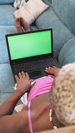 person relaxing on a couch while using a laptop with a green screen