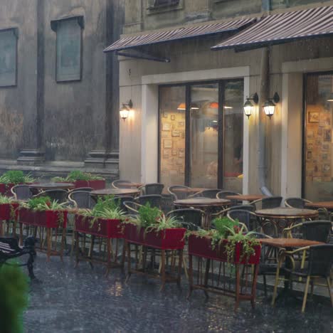raindrops are falling on the tables and chairs of the restaurant on the street. wet summer terrace with flower pots is near the road