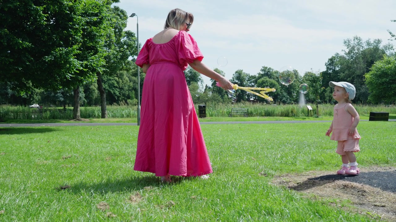 Nærbilde i sakte film: Bestemor og ung barnebarn leker med såpebobler i en solrik park, og fanger glade familieøyeblikk mellom generasjonene
