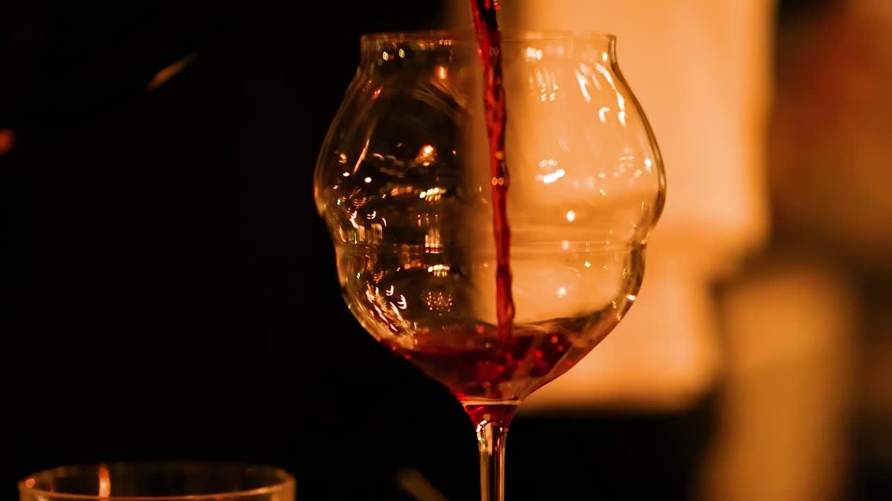 A close-up view of red wine being poured into a glass, set against a warmly lit background.