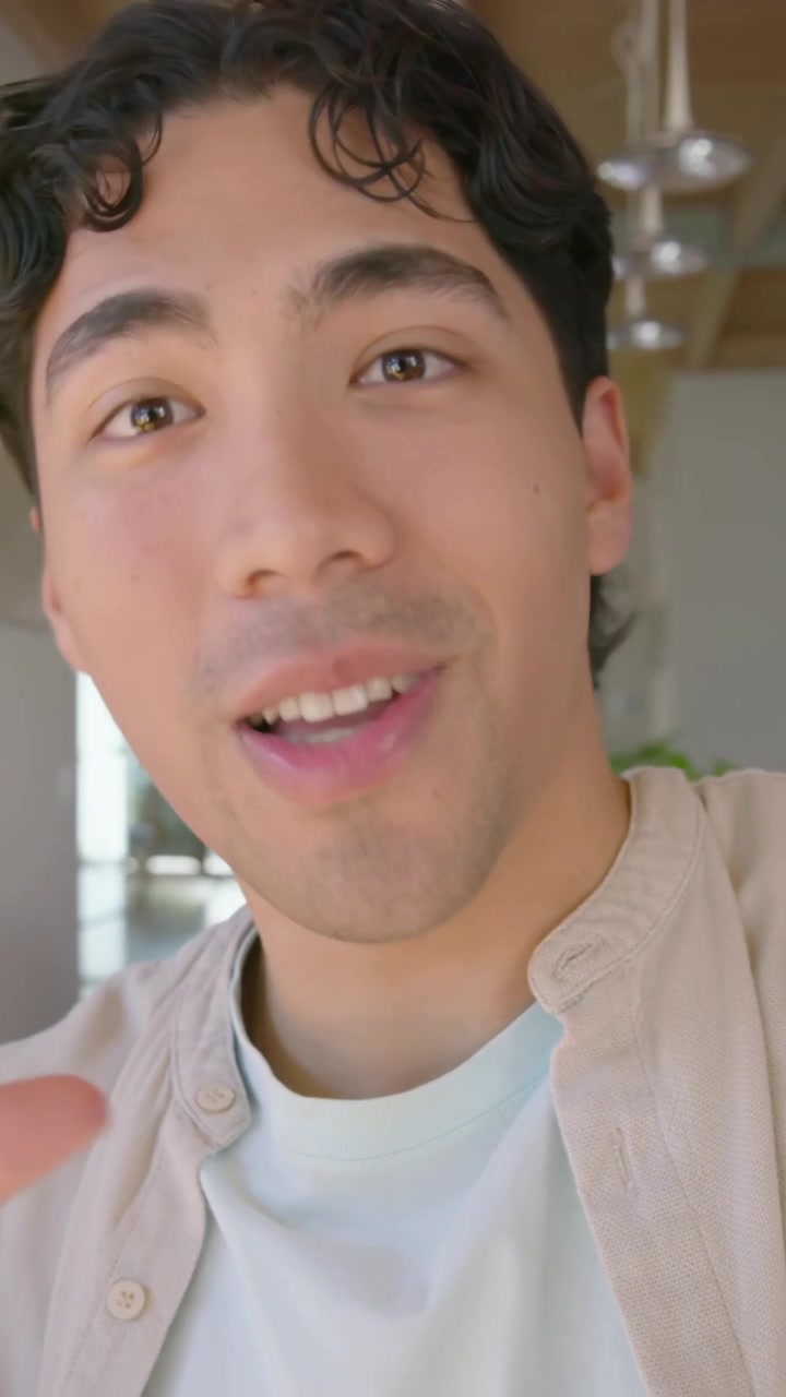 Video verticale: Uomo che registra usando lo smartphone, indossando una sovracamicia beige, sottolineando un punto a casa.