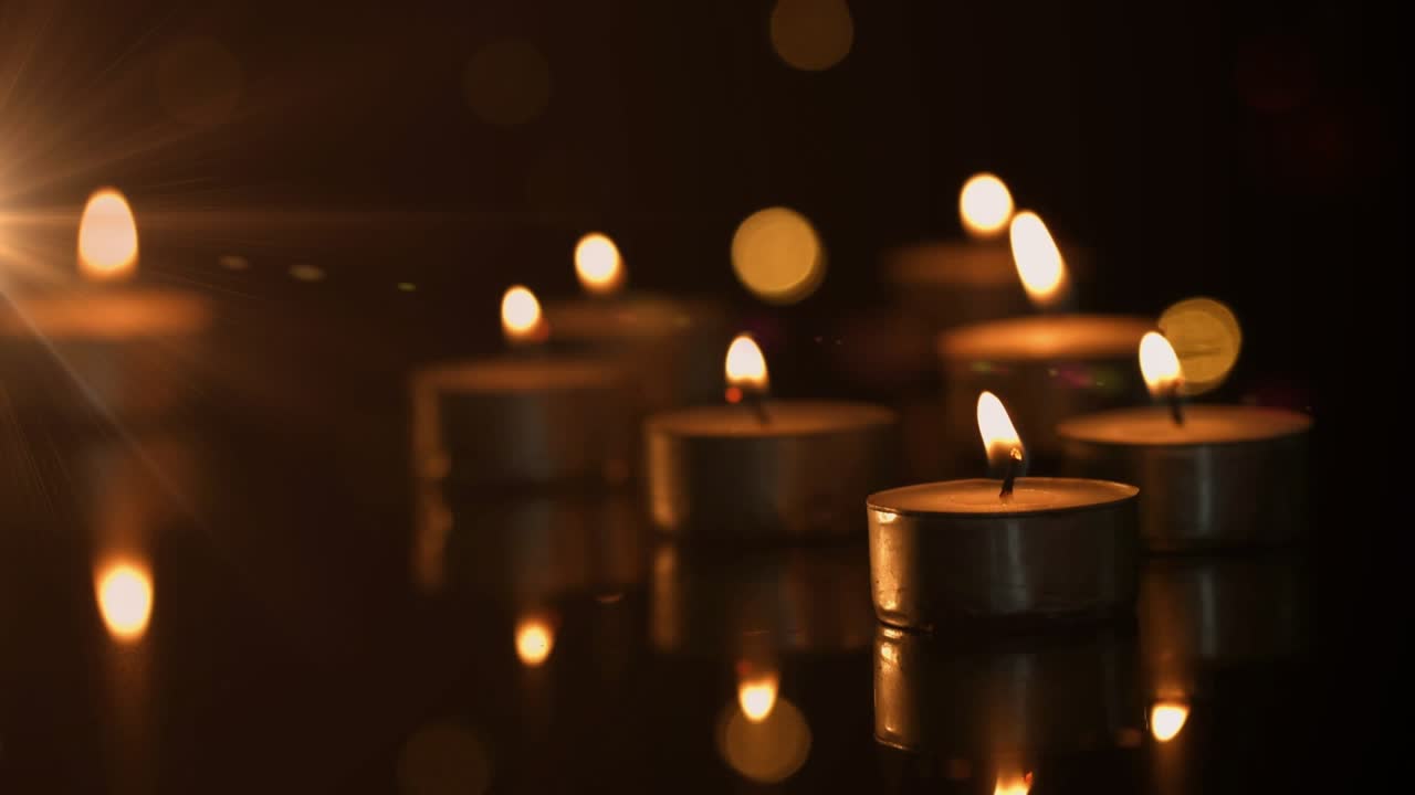 Low-angle view shows tea light candles flickering and mirroring tabletop evoking calm meditation