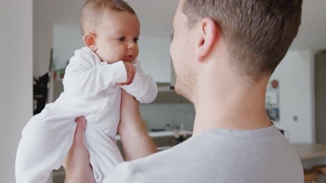 loving father lifting 3 month old baby daughter in the air in kitchen at home