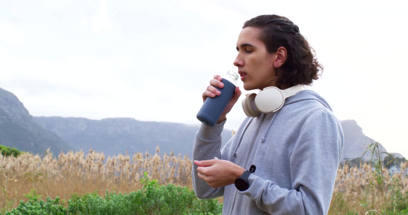 Uomo adulto afroamericano che ripara telefoni tra le canne prima di aprire una bottiglia e bere acqua, con spazio per il testo