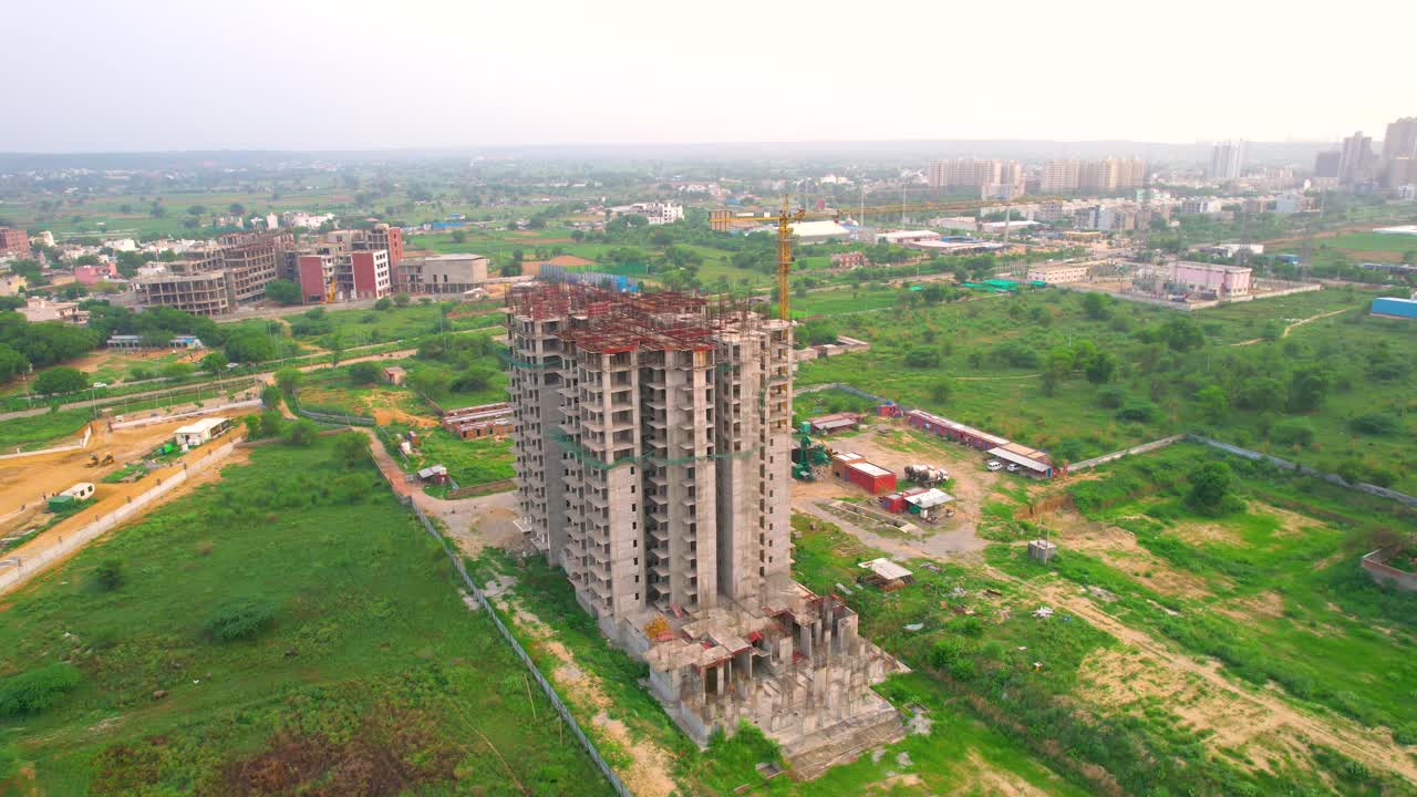 Aerial drone shot orbiting under construction building with exposed concrete, green safety nets and rooftop crane showing building house in middle of nature