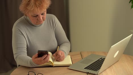 close up wrinkled male hands writing information. old mature woman working at office, using computer, handwriting notes