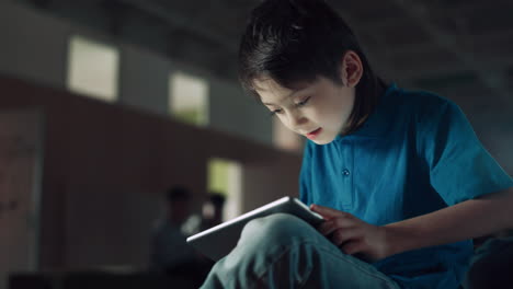 excited boy playing online game holding tablet in school hall. guy sitting bench