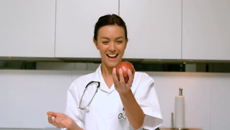 Home-nurse-throwing-and-catching-apple-and-smiling-in-kitchen