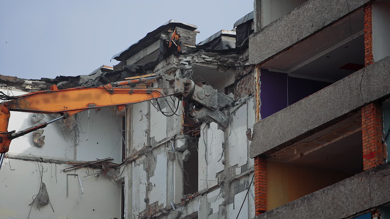 Demolishing machine claw tries to grab the concrete block to tear it off. Excavator working at dismantling the ruined house.