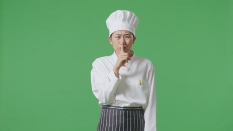 asian woman chef looking at camera and making shh gesture in the green screen background studio