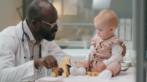 african american pediatrician playing with caucasian baby in clinic