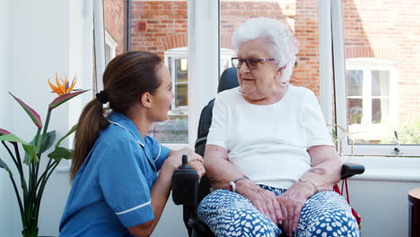 Senior-Woman-Sitting-In-Motorized-Wheelchair-Talking-With-Nurse-In-Retirement-Home