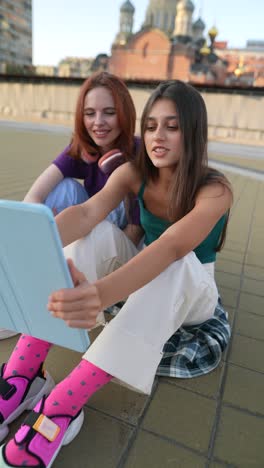 two young women using a tablet on a rooftop