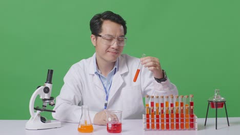 asian man scientist looking at test tube then smiling and showing thumbs up gesture while working on the table with microscope in the green screen background laboratory