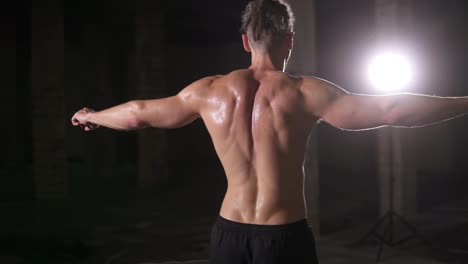 strong bodybuilder posing backside after training with spotlight lens flare - showing his body and muscles spreading the hands