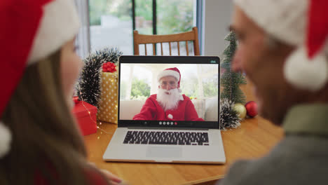 Rückansicht-Eines-Kaukasischen-Paares-Mit-Weihnachtsmützen,-Das-Während-Der-Weihnachtszeit-Einen-Videoanruf-Auf-Dem-Laptop-Führt