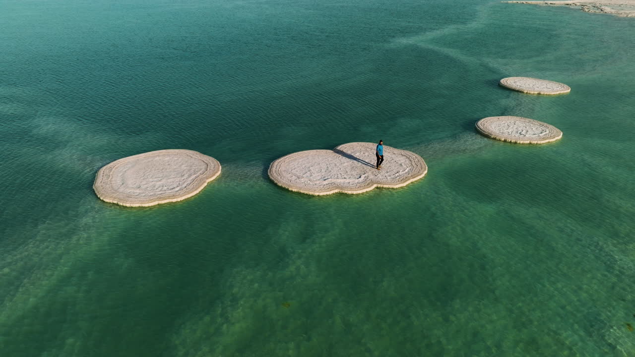 человек на расстоянии ходит босиком по солевому образованию в солнечный день в мертвом море, израиль