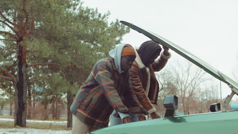 african american friends looking under car hood and speaking