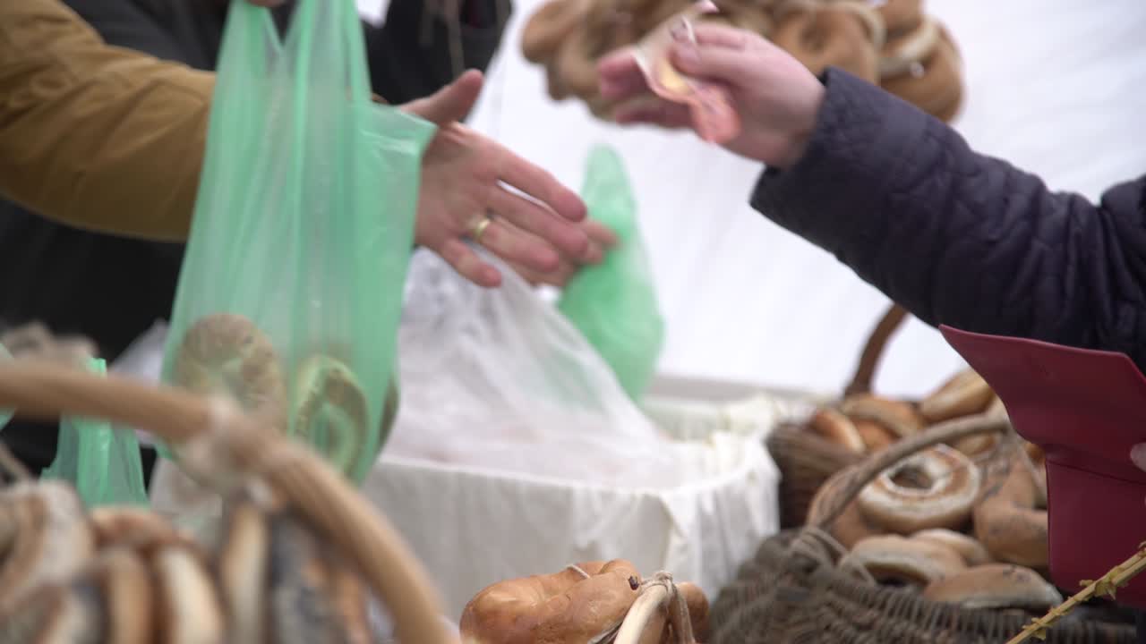 костюмер покупает хлебные рулоны в форме кольца, приправленные маковыми семенами, в городском билете. рука платит деньги за булочки, хлебное кольцо