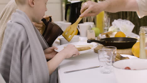 happy man serving fried eggs to his family while they having breakfast at camping in the forest